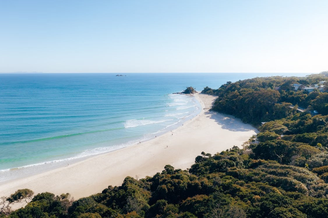 Pristine white sand beach and coastal luxury homes framed by lush greenery during a luxury stay at Byron Bay.