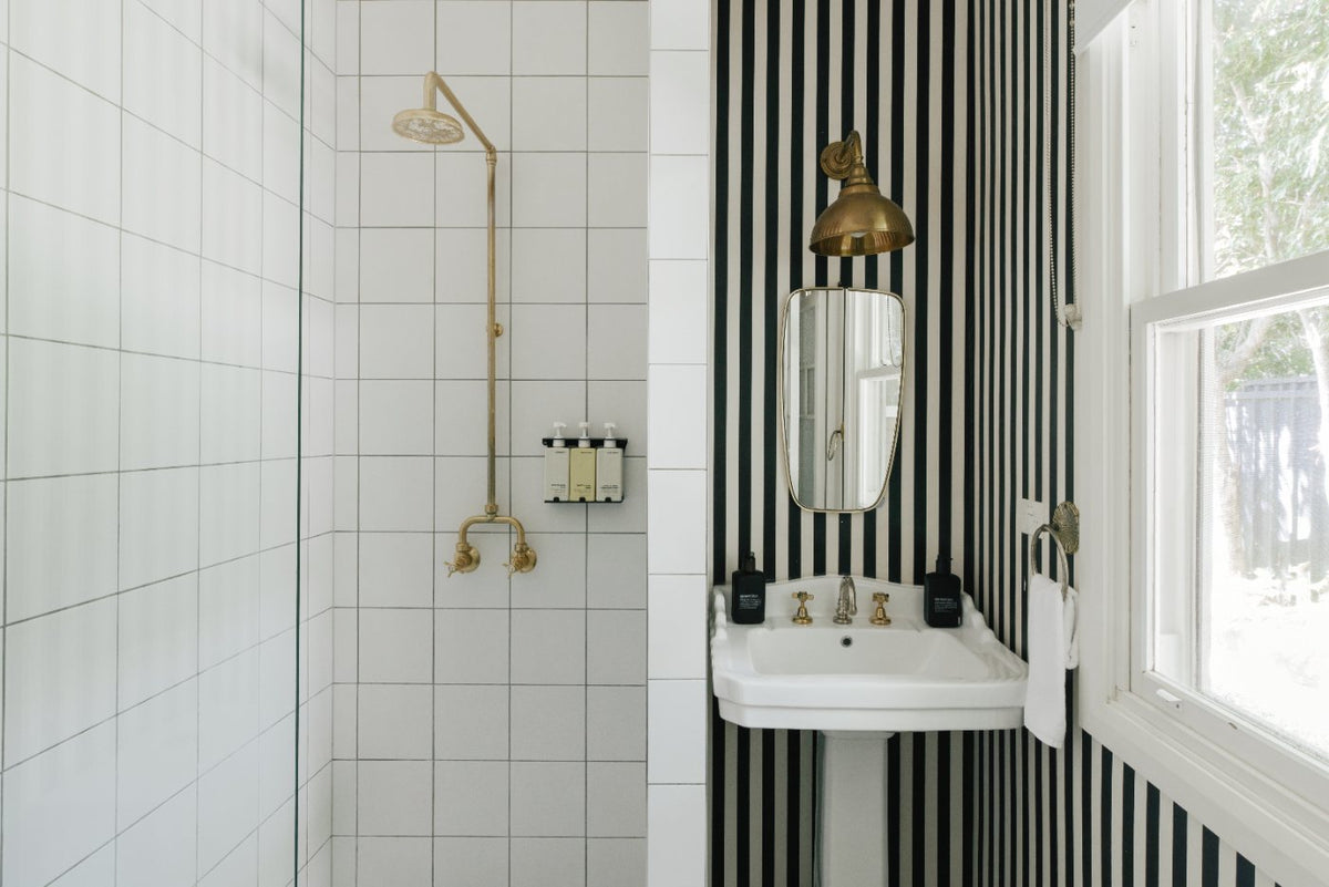 Striped bathroom with a brass shower and pedestal basin