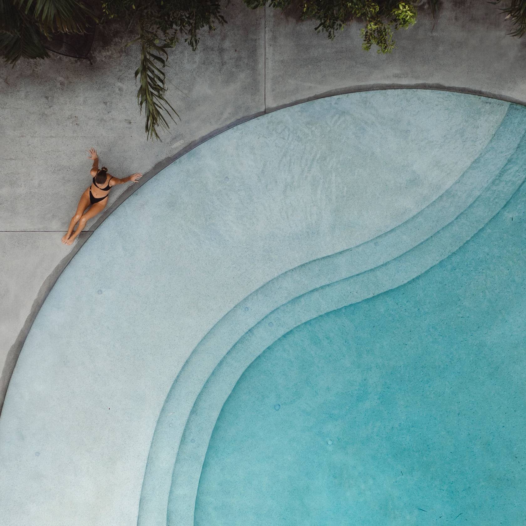 Person lounging by a pool with palm trees in the background